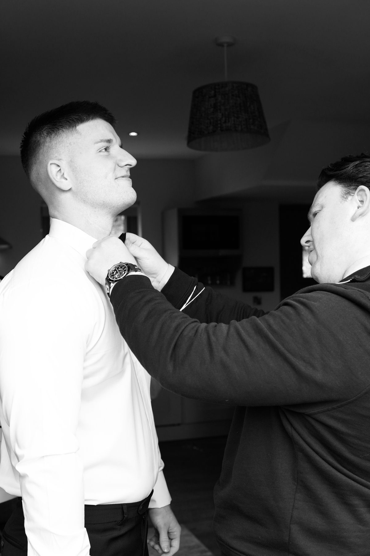Raymond straightening a groomsman’s bow tie at the collar.