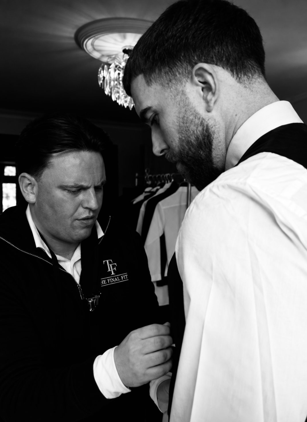 Raymond setting a groomsman’s collar and tie under a chandelier.